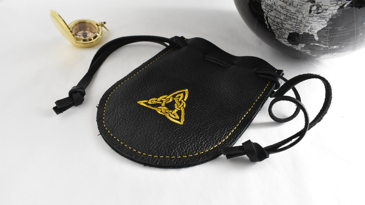 pouch with gold triangle embroidered on it. there is a globe and compass sitting nearby.
