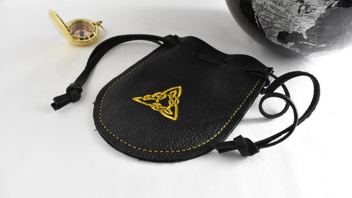 pouch with gold triangle embroidered on it. there is a globe and compass sitting nearby.